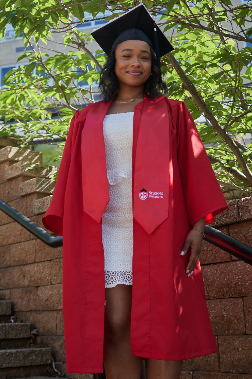 Closer portrait in cap and gown under green trees.