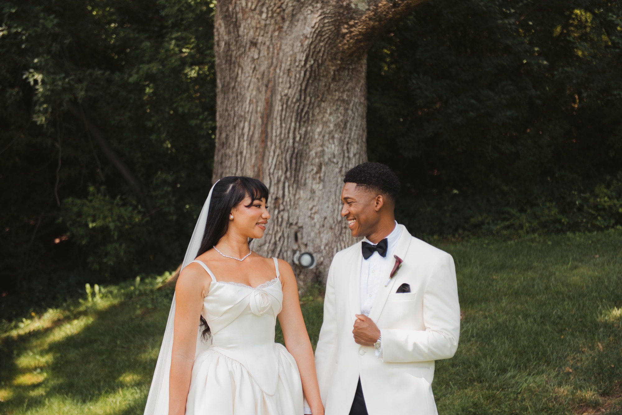The couple smiling at each other in front of an old oak tree.